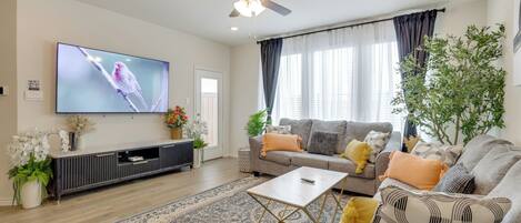 Een moderne woonkamer met een flatscreen televisie, een plafondventilator, een zithoek, een salontafel en een decoratief vloerkleed.