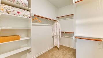 A walk-in closet with white shelving, a wooden coat rack, and a beige carpet.