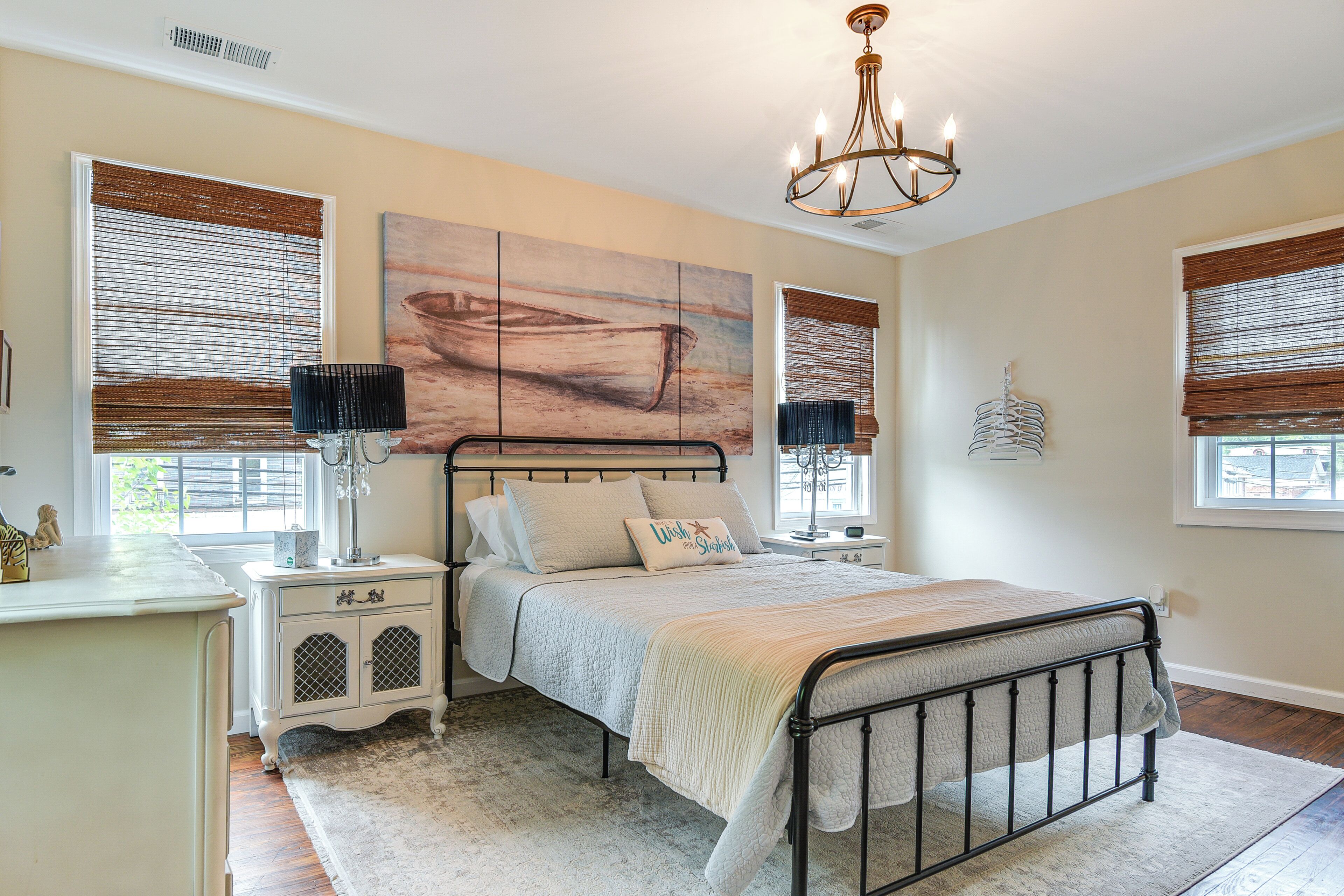 A bedroom with a bed, bedside tables, a chandelier, and artwork on the wall.