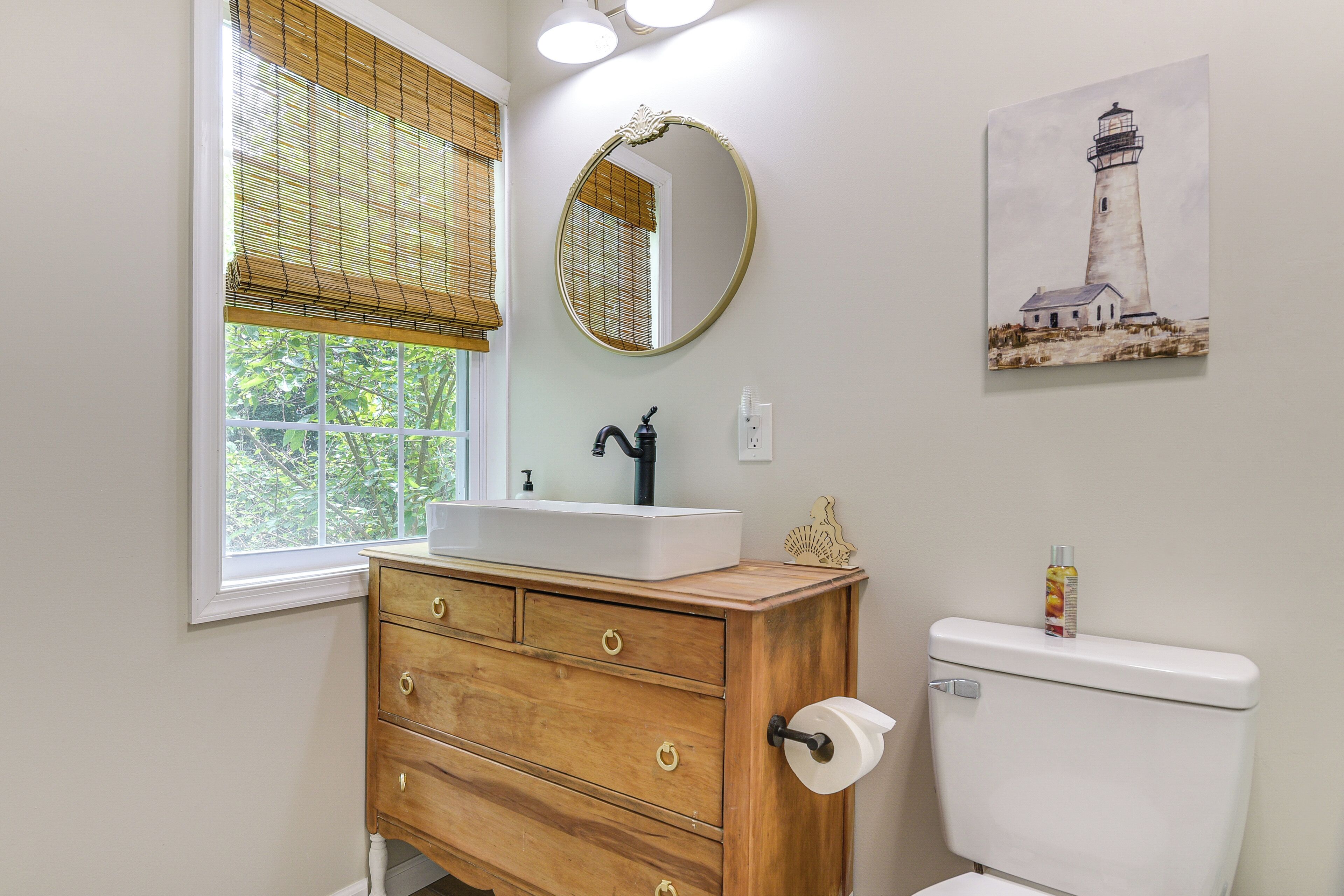 Un baño con tocador de madera, un lavabo blanco, un espejo redondo y un inodoro.