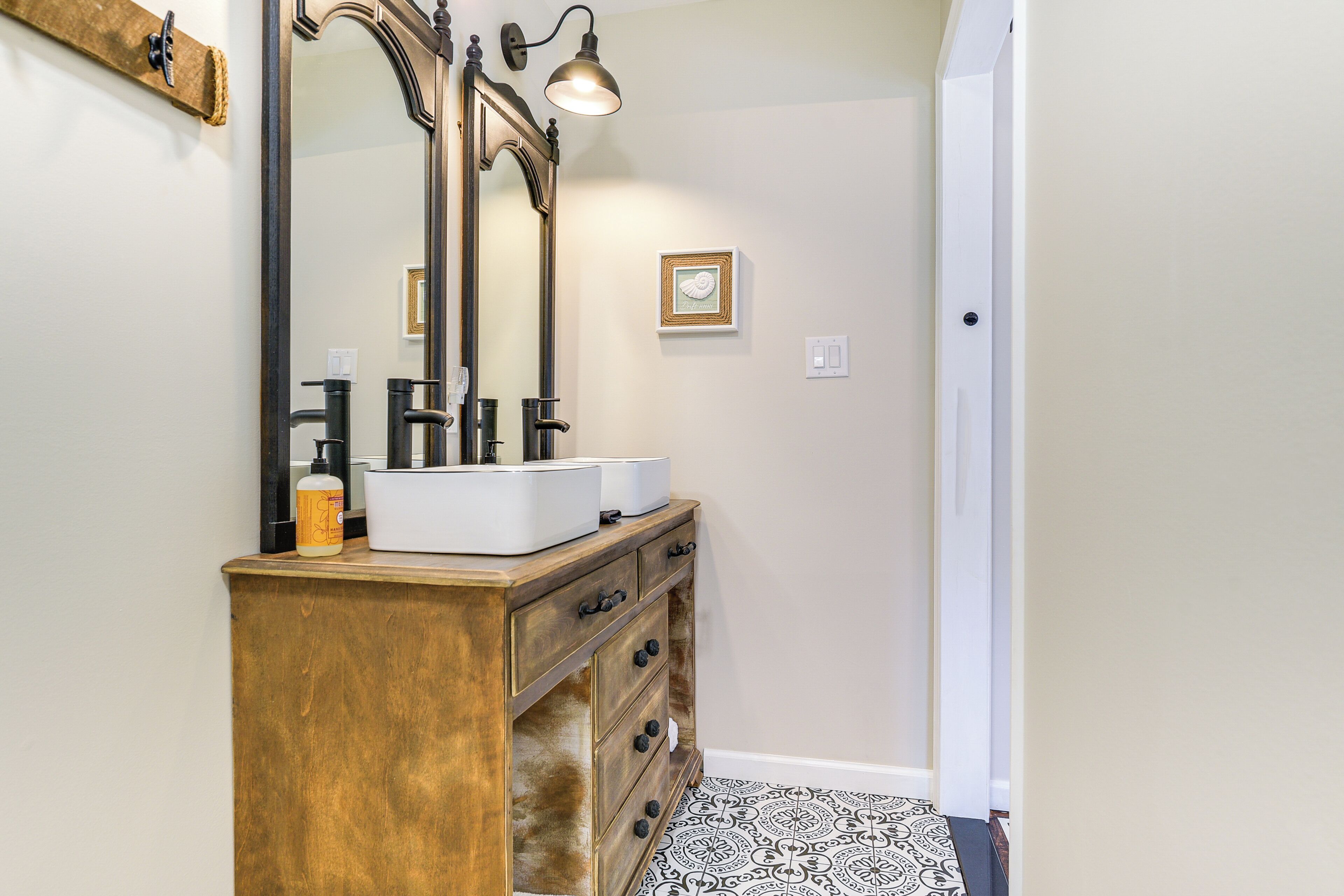 A bathroom with a wooden vanity, two sinks, a large mirror, and a wall-mounted light fixture.