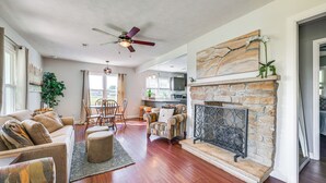 A spacious living room with hardwood floors, a fireplace, a ceiling fan, and a dining area with a table and chairs.