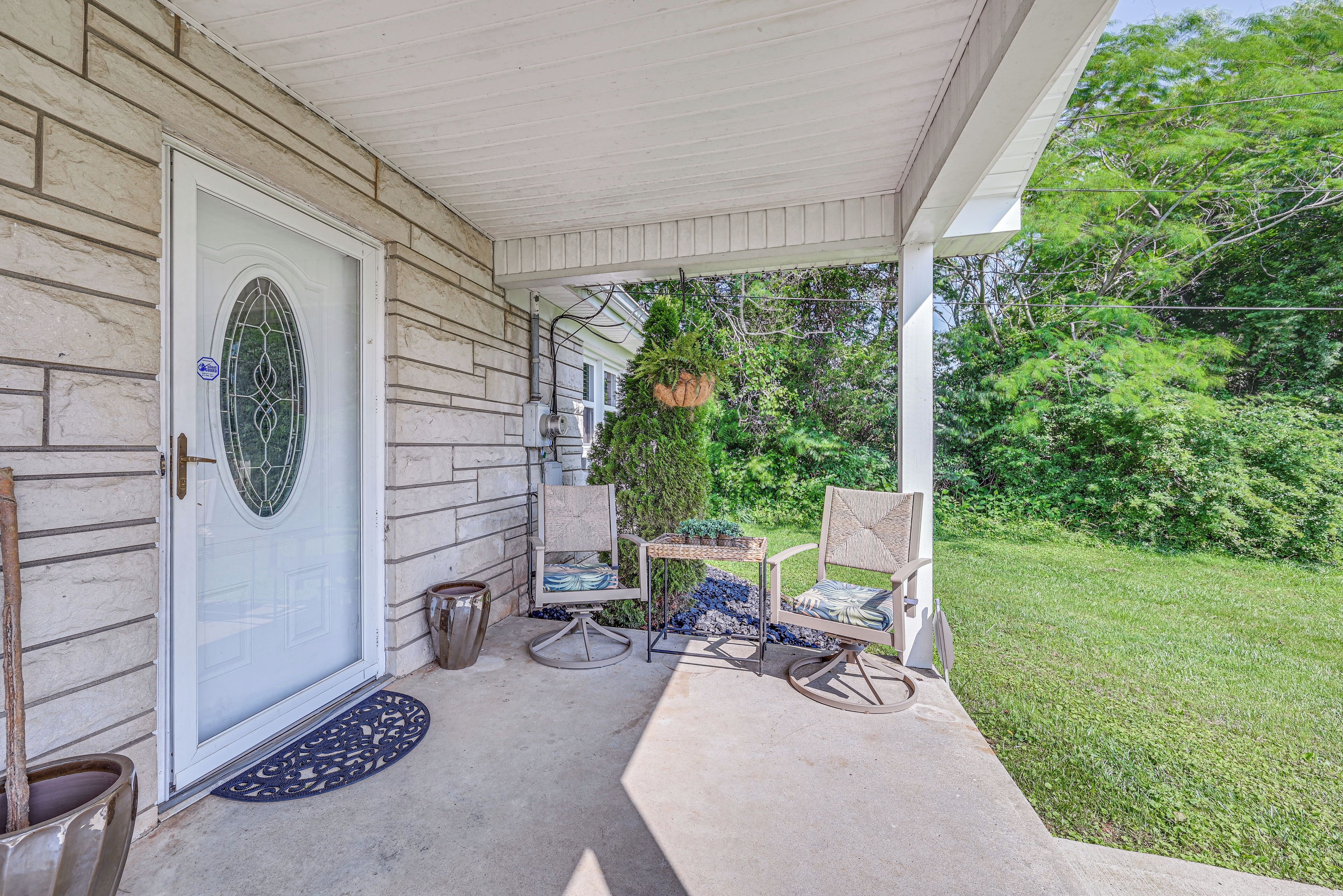A covered porch with a white door, two rocking chairs, a small table, and a hanging planter.