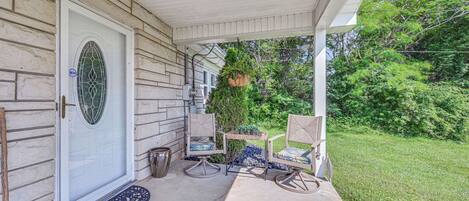A covered porch with a white door, two rocking chairs, a small table, and a hanging planter.
