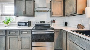 A kitchen with wooden cabinets, a stainless steel stove, a microwave, and a window with blinds.