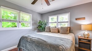 A bedroom with a bed, a ceiling fan, a nightstand, and a window with blinds.