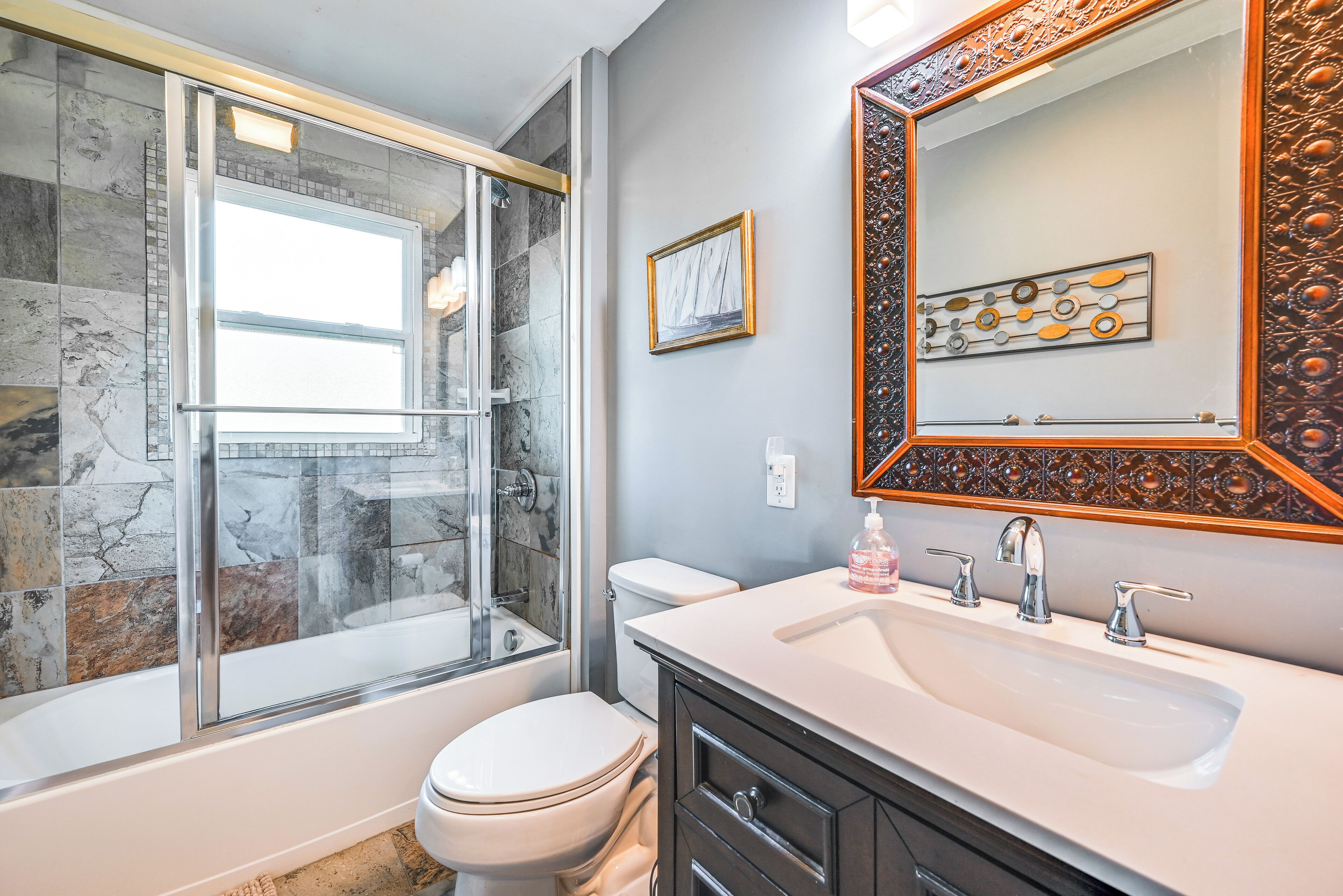 A bathroom with a glass-enclosed shower, a white toilet, a sink with a mirror, and decorative tiles.