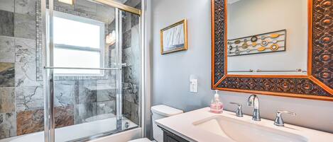 A bathroom with a glass-enclosed shower, a white toilet, a sink with a mirror, and decorative tiles.