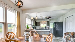 A dining area with a wooden table and chairs, a vase with flowers, and a view of the kitchen and outdoor space.
