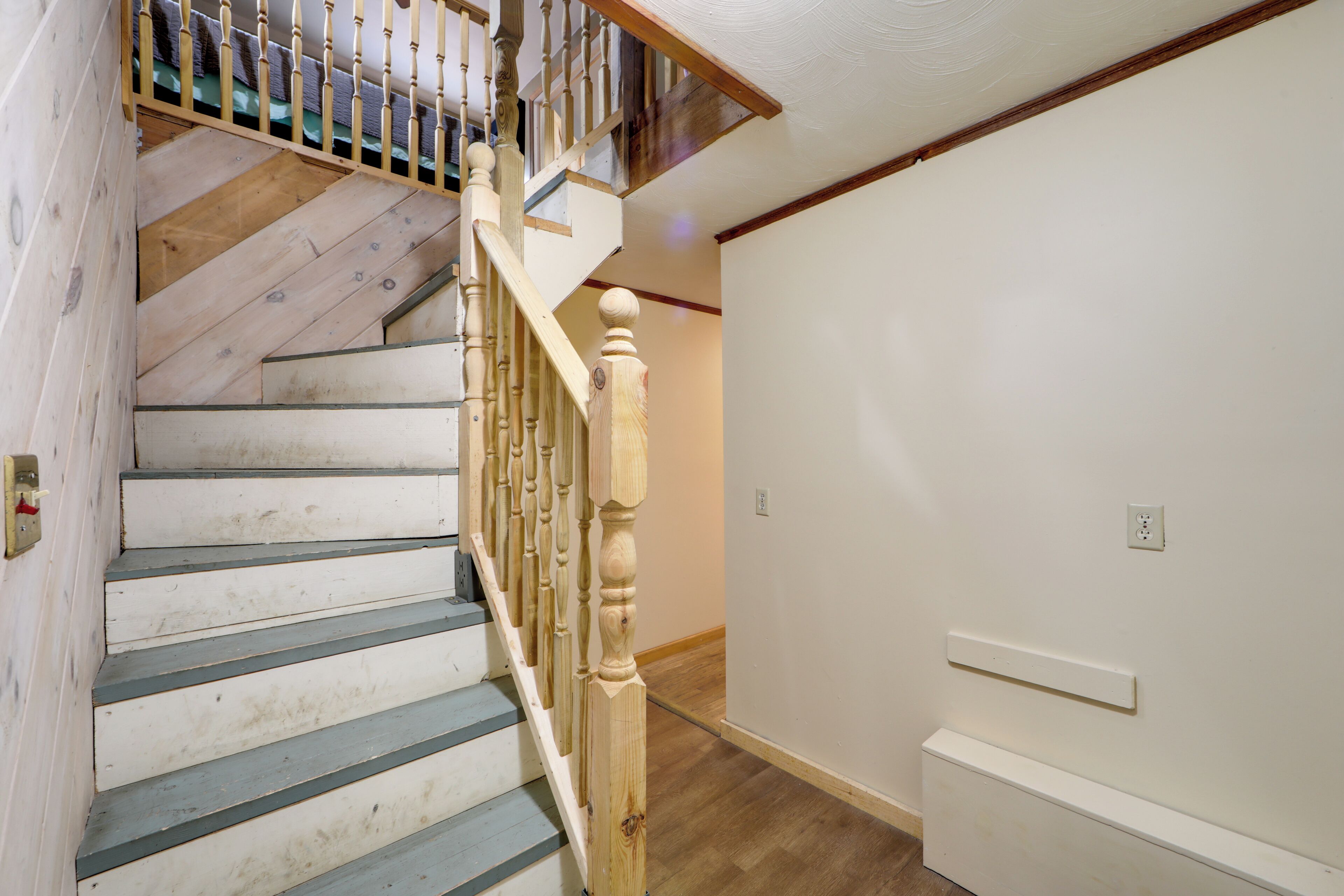 Eine Treppe mit Holzbeschlägen und einem Holnänder, die zu einer Zwischenebene mit einer weißen Wand und einem Lichtschalter führt.