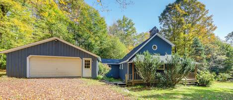 A two-story house with a garage, surrounded by trees and a gravel driveway.
