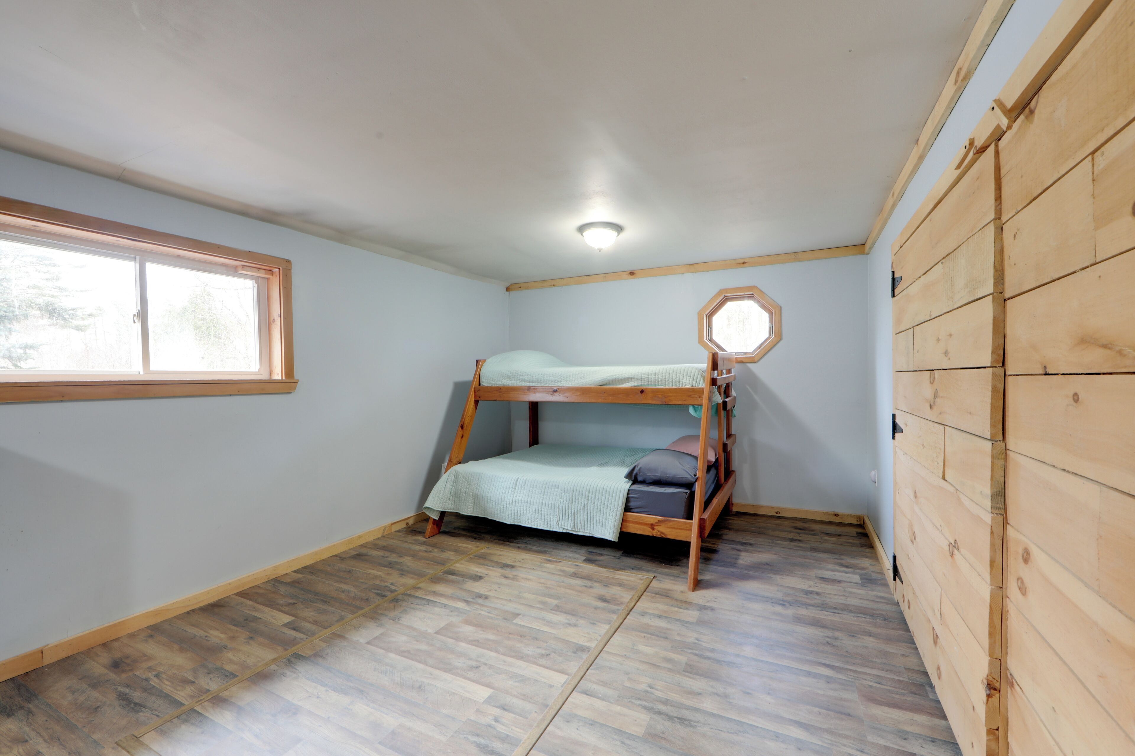 Dormitorio con literas, ventana, paredes de madera y una lámpara en el techo.