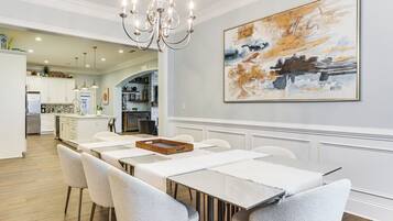 A modern dining area with a long table and chairs, a chandelier, and a large abstract painting on the wall.