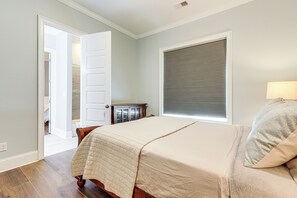 Une chambre à coucher comprenant un lit, une table de chevet, une lampe, une fenêtre avec des stores et une porte donnant sur une autre pièce.