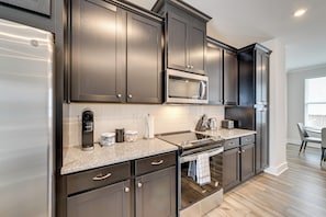 A modern kitchen with dark cabinets, stainless steel appliances, a granite countertop, and a dining area with a table and chairs. - 2 Mi to Uptown Charlotte: Family Townhome! (Charlotte)