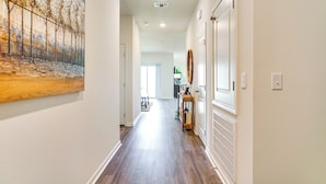 A hallway with wooden flooring, white walls, and a large abstract painting on the left. - 12 Mi to Avery Island: Spacious Family Home! (New Iberia)