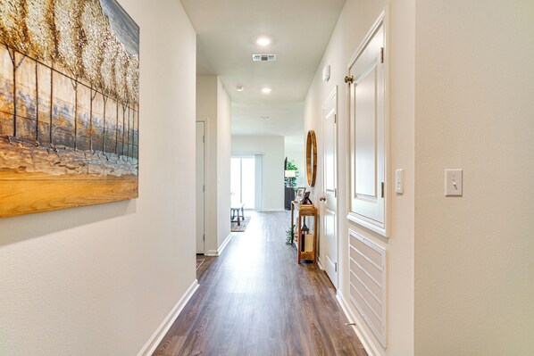 A hallway with wooden flooring, white walls, and a large abstract painting on the left.