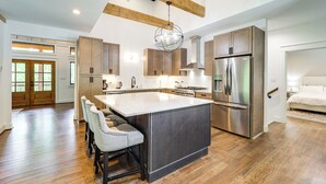 Une cuisine spacieuse dotée d’un grand îlot central, de poutres en bois au plafond et d’appareils électroménagers en acier inoxydable.