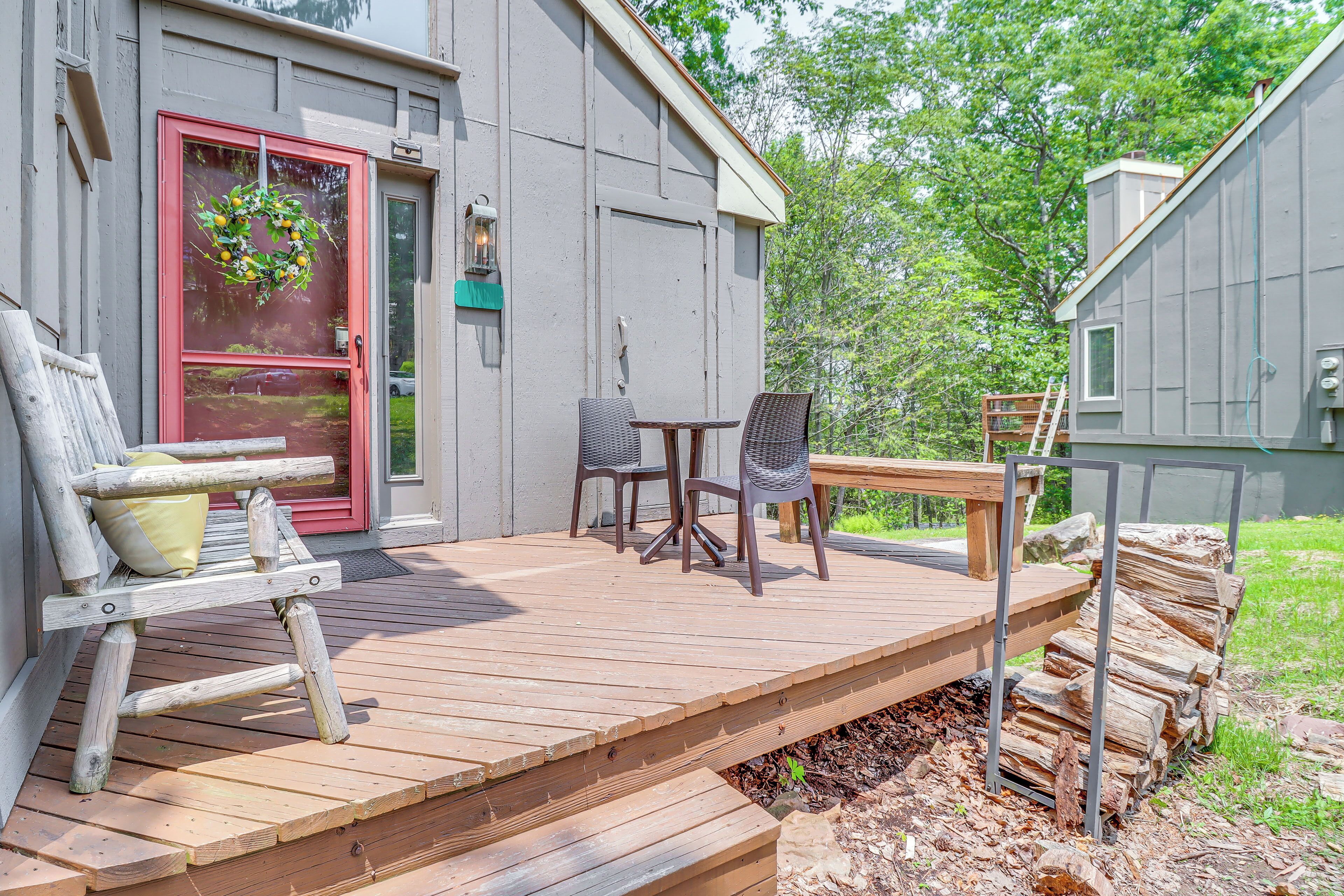 Une terrasse en bois avec un banc et des chaises, une porte ornée d’une guirlande et une petite table.