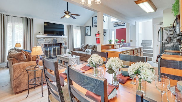 A spacious living area with a fireplace, a dining table set with chairs, and a television mounted on the wall.