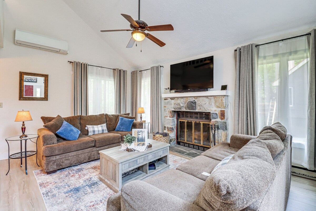 A living room with a sofa set, a coffee table, a fireplace, a flat-screen TV, and a ceiling fan.