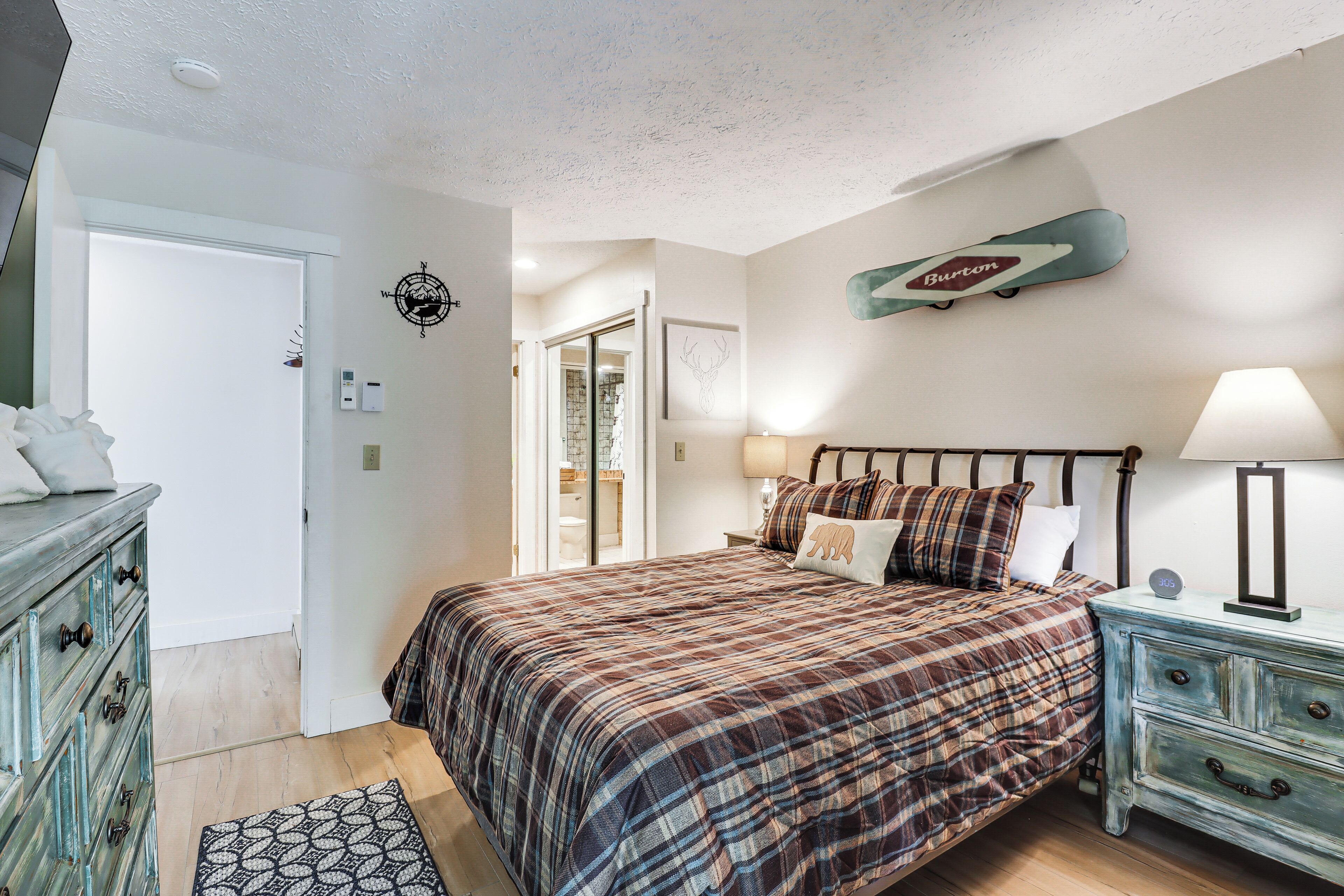 A bedroom with a plaid bedspread, a dresser, a lamp, and a wall-mounted skateboard.