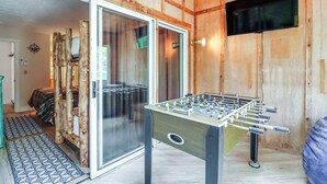 A room with a wooden interior, a foosball table, and a sliding glass door leading to another room.