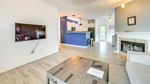 Een ruime woonkamer met een houten salontafel, een aan de muur bevestigde televisie en een openhaard op de achtergrond.