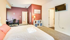 Een hotelkamer met een groot bed, een bureau met stoel, een aan de muur bevestigde televisie en een deur naar een andere kamer.