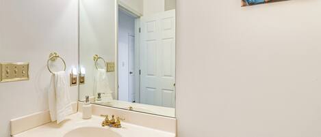 Un baño con un lavamanos blanco, grifos dorados, un espejo grande y una puerta blanca al fondo.