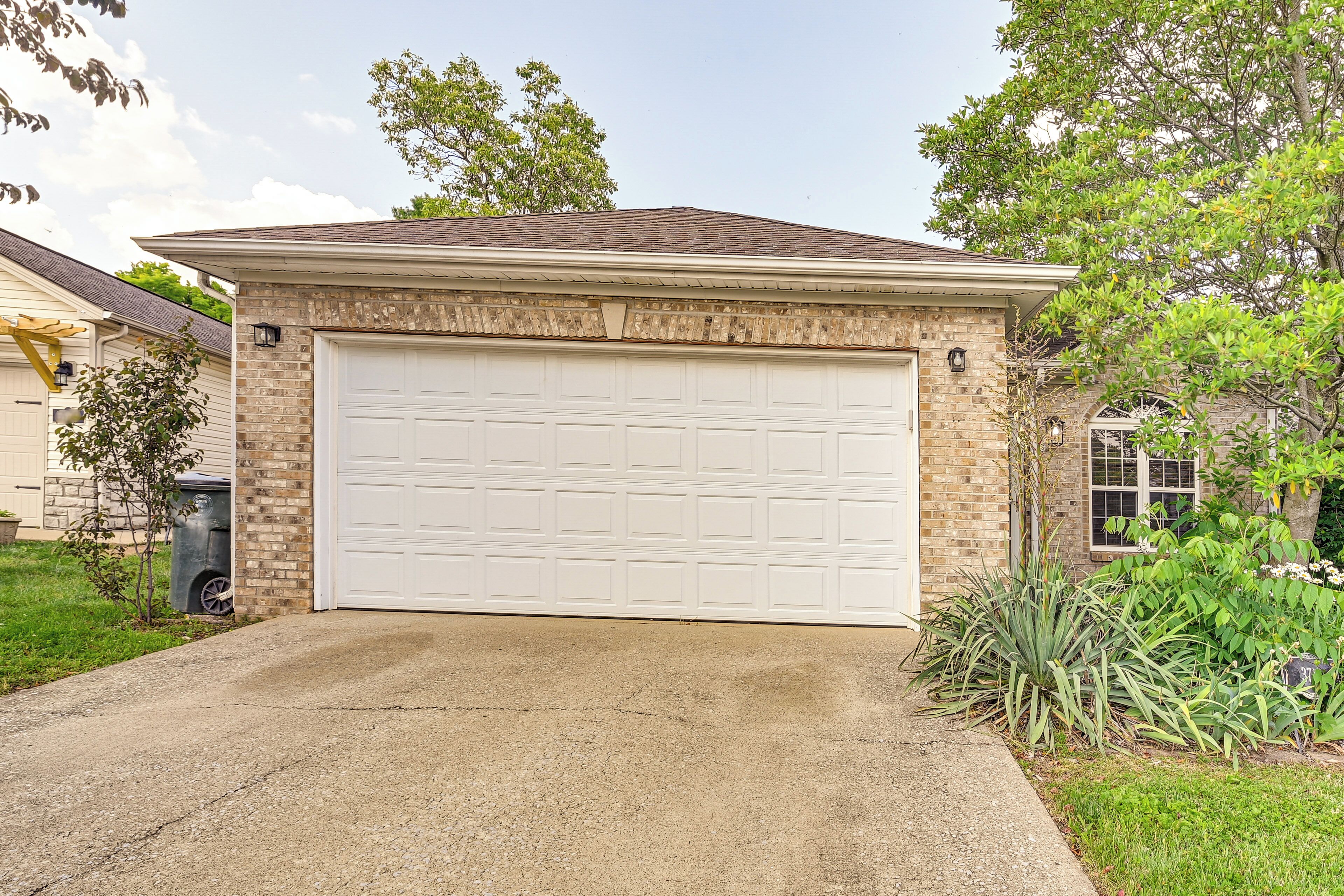A residential garage with a white door, brick facade, and a concrete driveway.