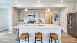 Una cocina moderna con armarios blancos, electrodomésticos de acero inoxidable y una isla central con taburetes.