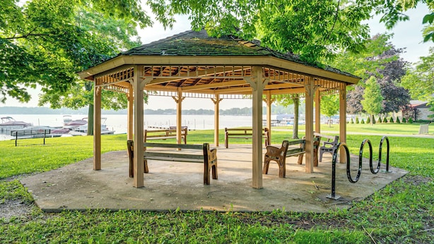 A gazebo with a tiled roof, surrounded by benches and a railing, overlooking a body of water.