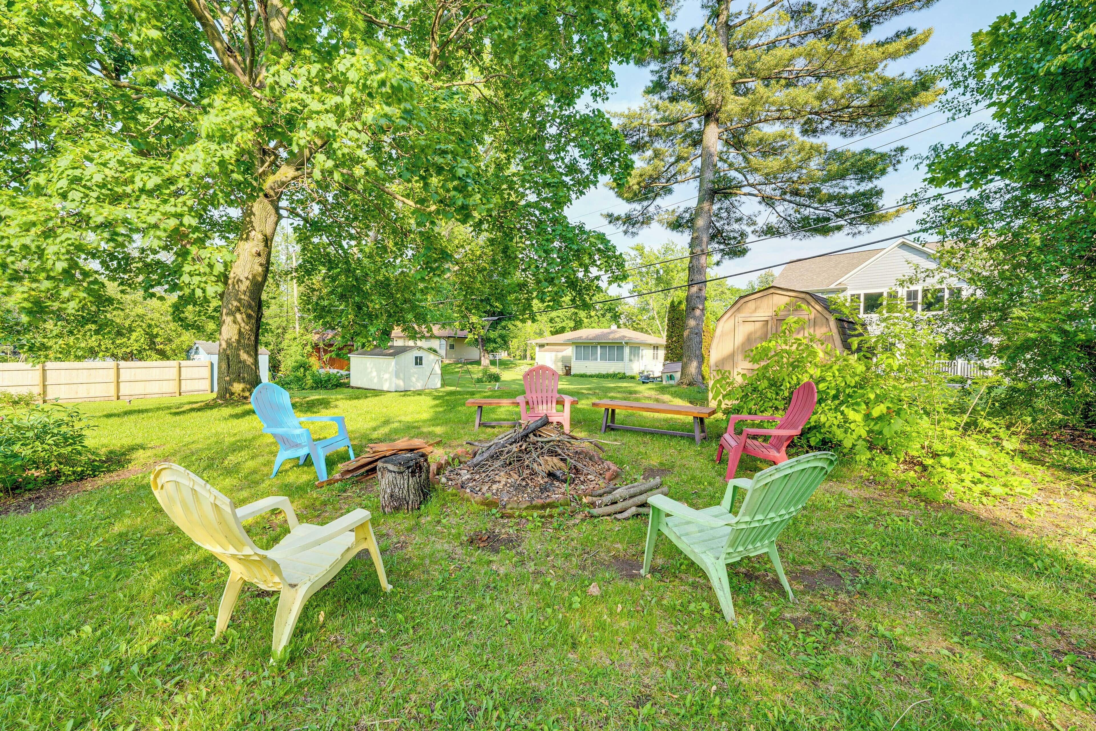 A backyard with a fire pit, green and red chairs, and a wooden deck.