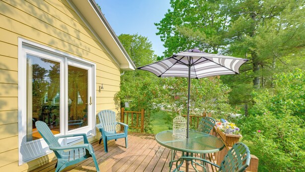 A wooden deck with a glass table and chairs, an umbrella, and a birdcage. - 1 Mi to Main St: Charming Elsworth Home w/ Yard! (Ellsworth)