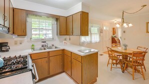A kitchen with wooden cabinets, a stove, a sink, and a dining table with chairs. - 1 Mi to Main St: Charming Elsworth Home w/ Yard! (Ellsworth)