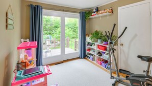 A room with a sliding glass door to a balcony, a pink playpen, a treadmill, and shelves with toys and plants. - 1 Mi to Main St: Charming Elsworth Home w/ Yard! (Ellsworth)