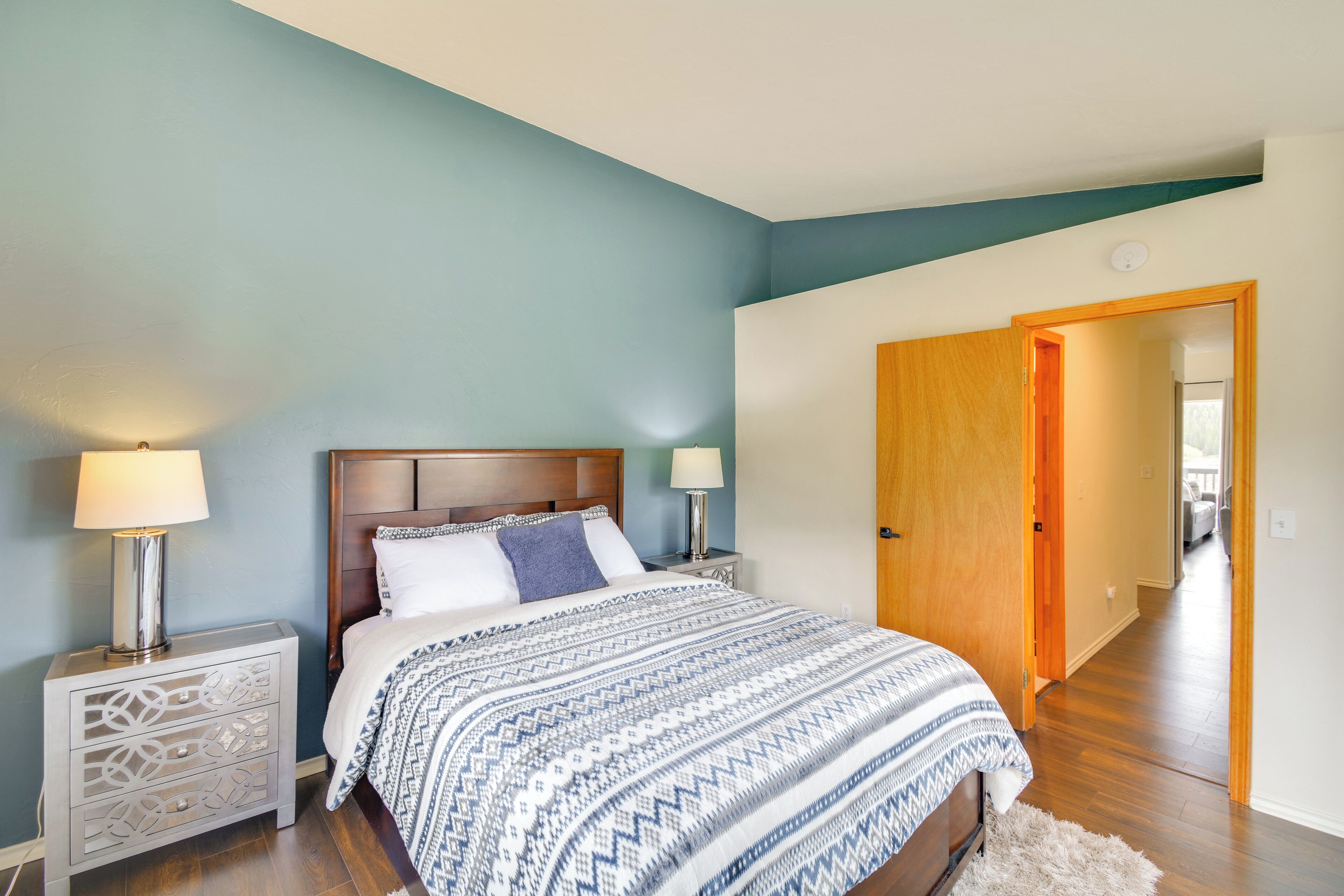 Quarto com cama, mesas de cabeceira e porta para outro cômodo.