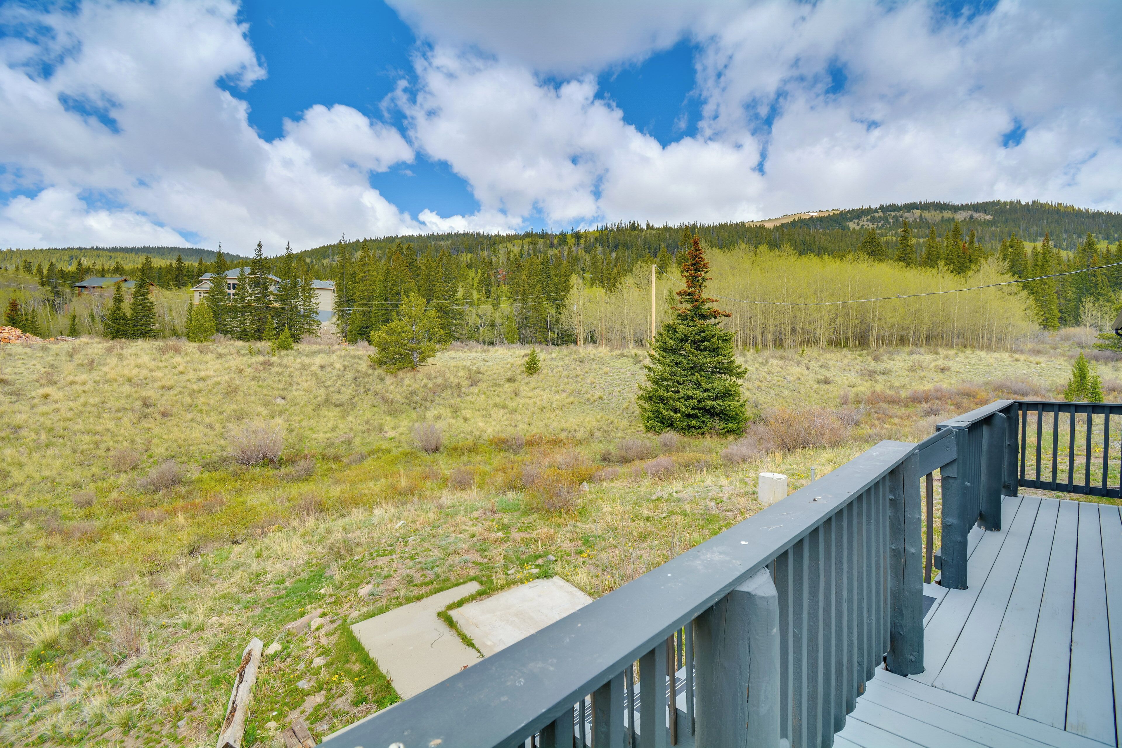 A wooden deck with a view of a grassy field, trees, and a mountain in the background.