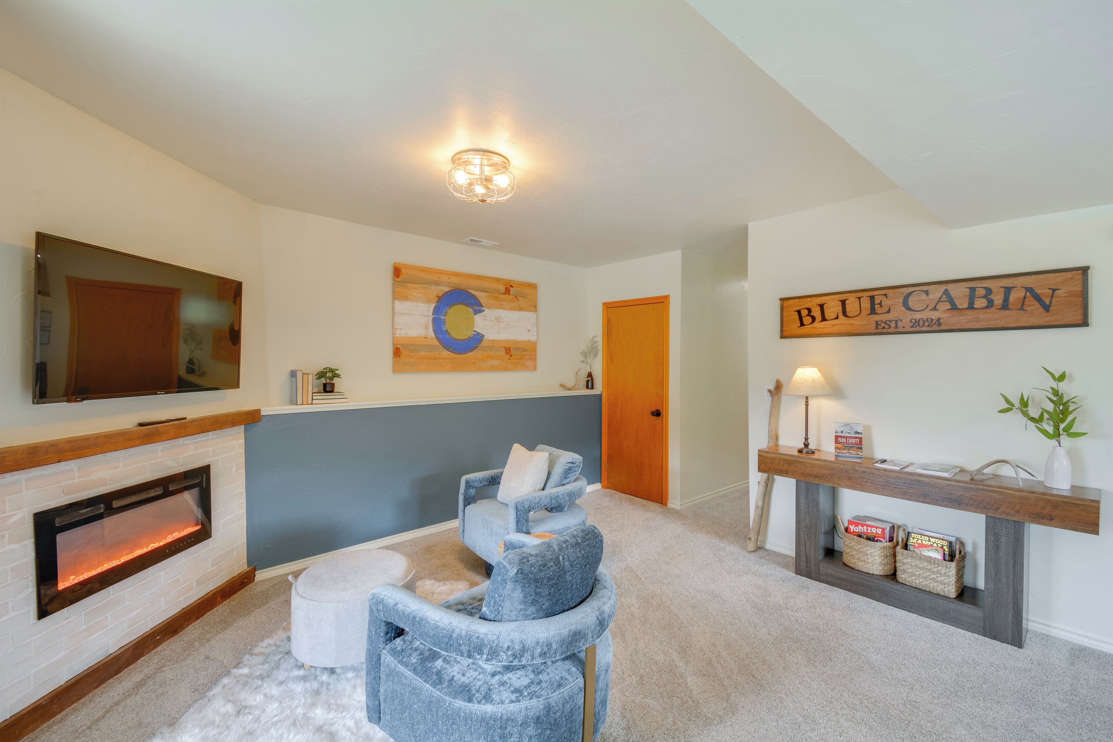 A living room with a fireplace, a television mounted on the wall, a blue couch, a wooden coffee table, and a sign that reads "BLUE CABIN EST. 2024".