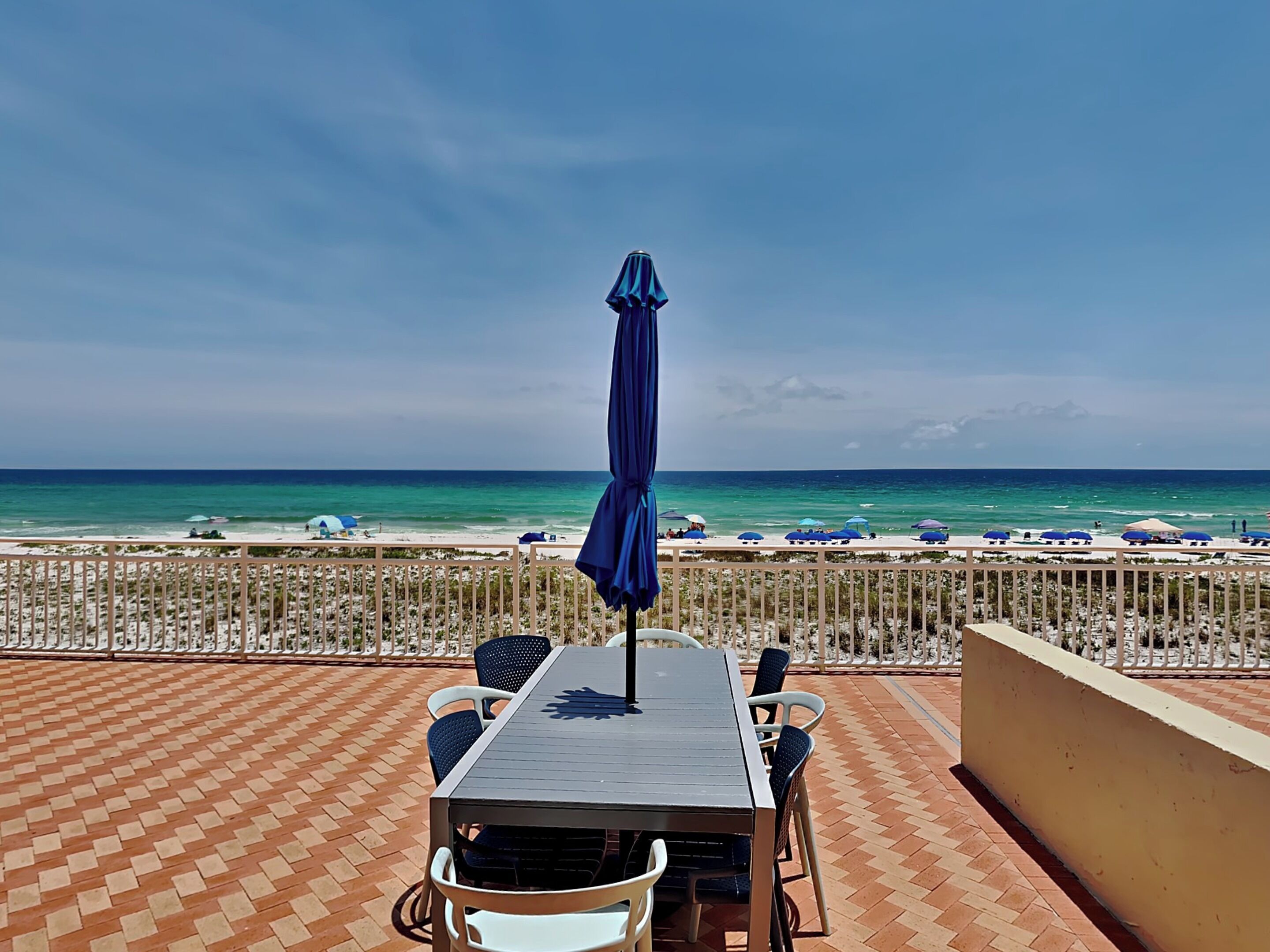 Eine Terrasse mit Tisch und Stühlen mit Blick auf einen Strand mit Sonnenschirmen und dem Meer.