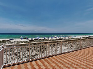 Uitzicht op het strand vanaf een balkon met betegelde vloer en een metalen hekwerk.