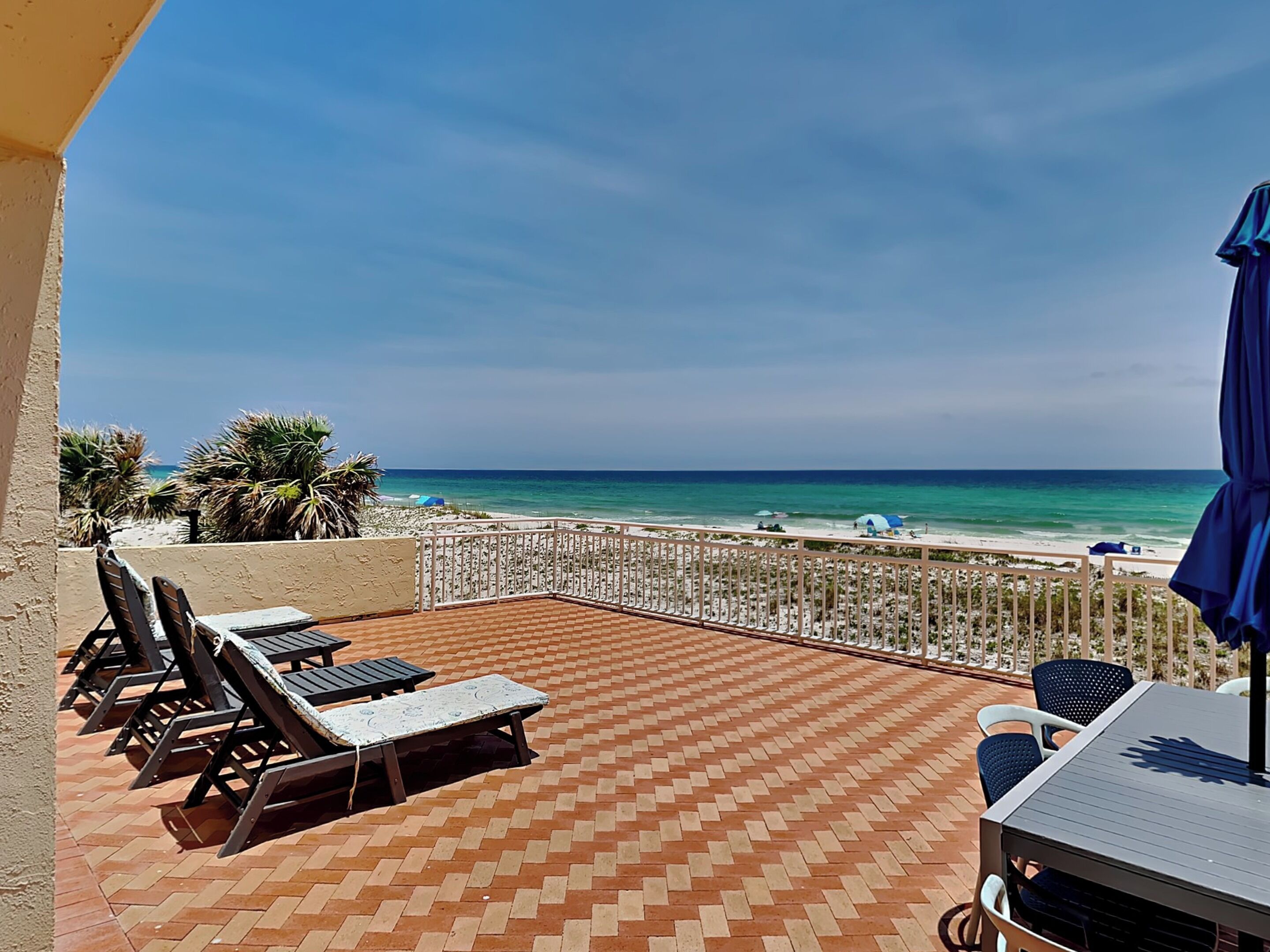 A terrace with a view of the beach, lounge chairs, and a table.