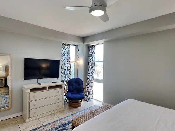 Ein Schlafzimmer mit Bett, Fernseher, Schminktisch, Stuhl und Deckenventilator.