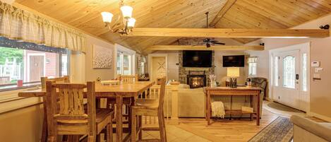 Un salón amplio con techo de madera, chimenea, televisor y comedor con mobiliario de madera.