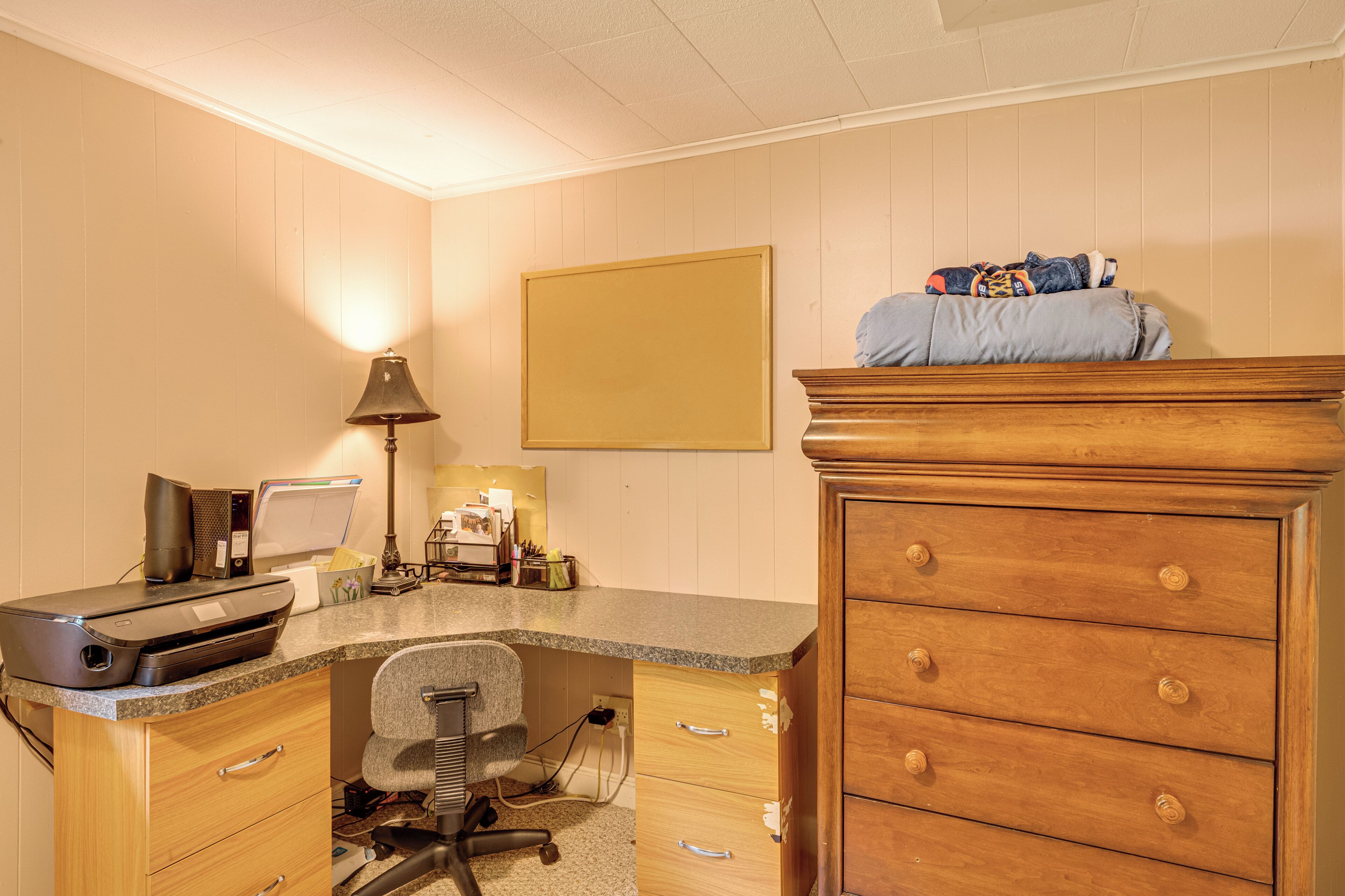 A home office with a desk, printer, lamp, and a dresser with drawers.