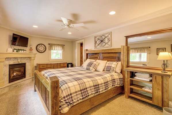 Une chambre à coucher avec un lit en bois, une cheminée, un ventilateur de plafond, un grand miroir et une fenêtre avec des rideaux.