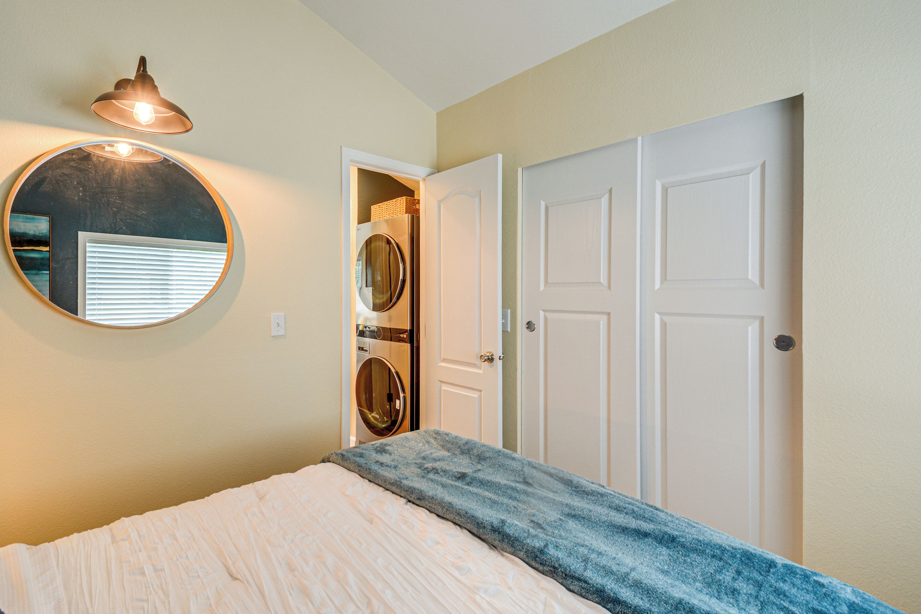 A bedroom with a bed, a circular mirror, a washing machine, and a door.