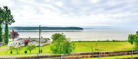 Une vue d’un lac, avec une clôture en bois au premier plan, une zone herbeuse et une maison en arrière-plan.