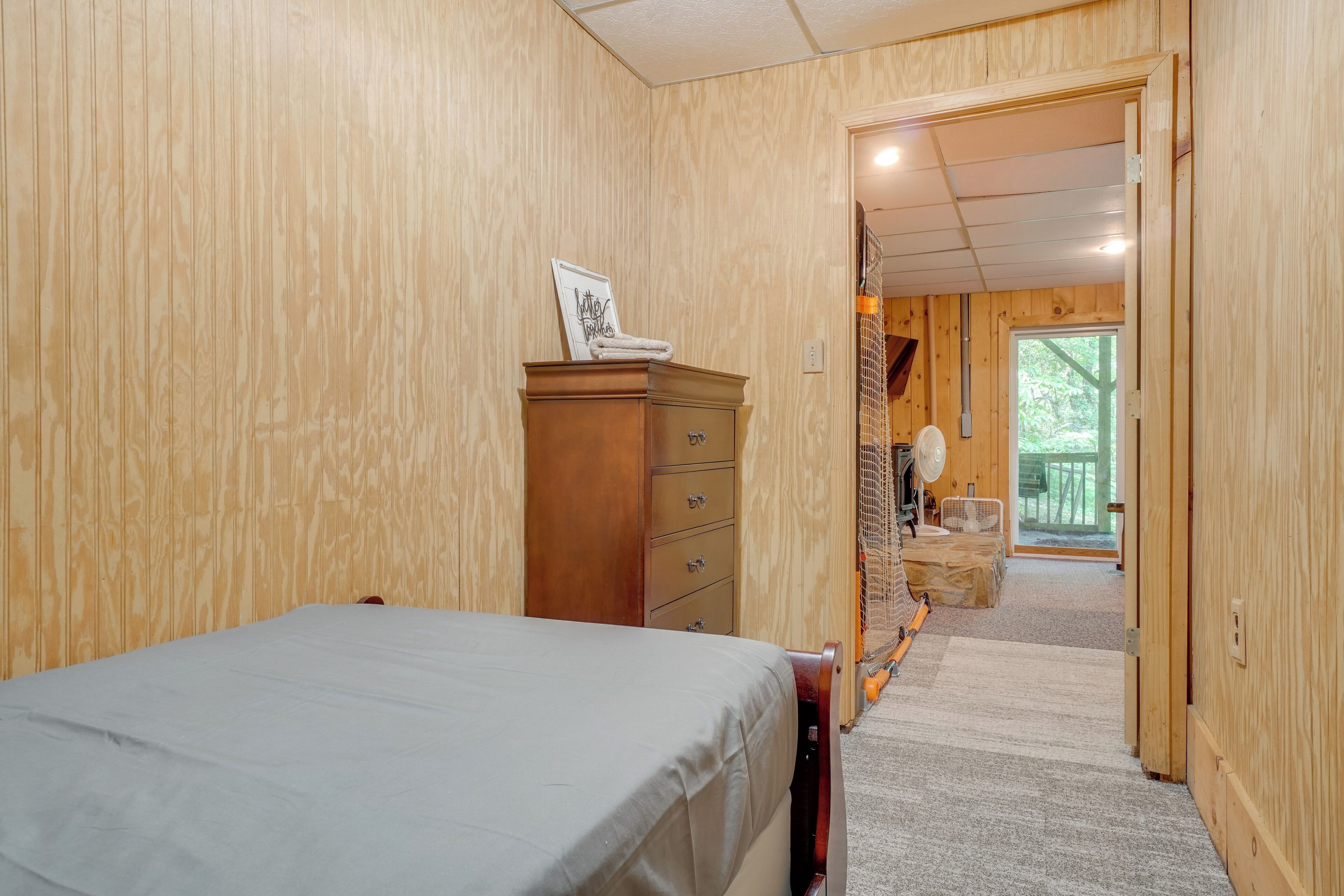 A wooden-paneled room with a bed, a wooden dresser, and a door leading to a balcony.